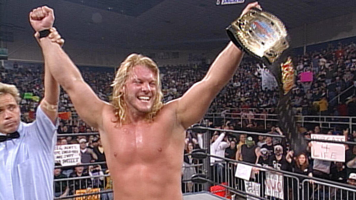 Jericho holds the Cruiserweight title in his left hand whilst the other is raised by the referee; Jericho smiles.