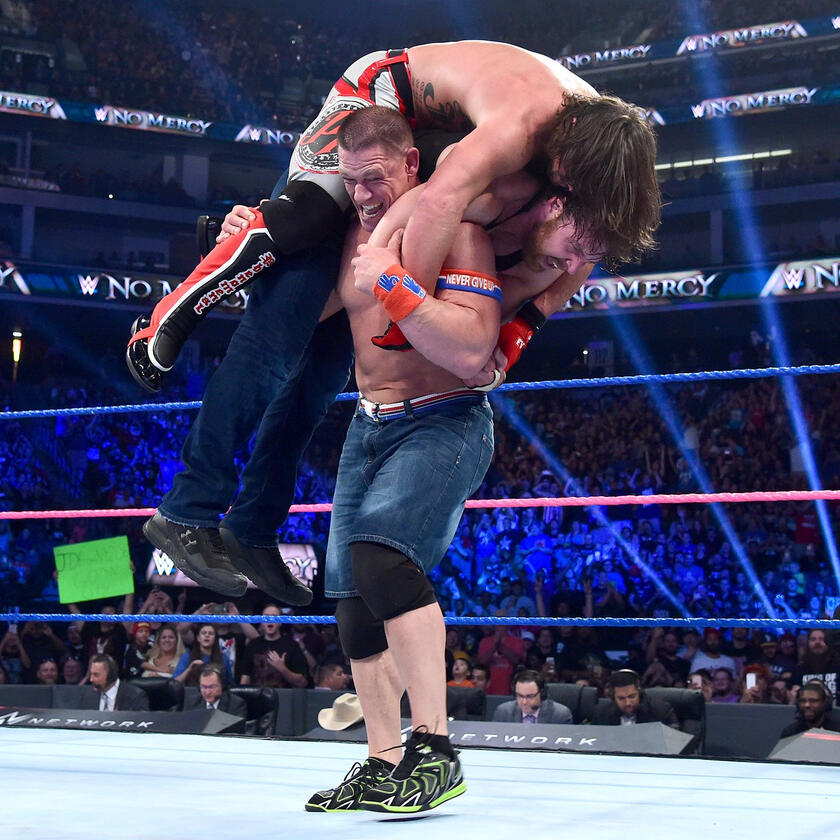 In a Herculean show of strength, Cena lifts both Styles and Ambrose atop his mighty shoulders.