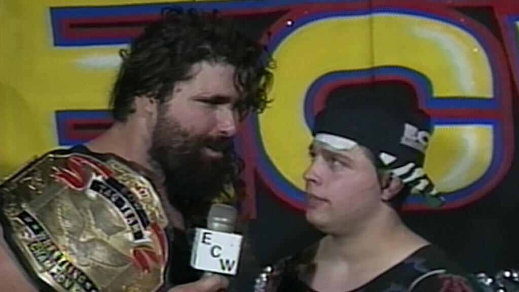 With one of the ECW World Tag Team titles on his shoulder, Foley cuts a promo whilst standing next to partner Mikey Whipwreck, who is adorned in a side-on baseball cap.